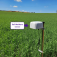 A Lacuna Space satellite IoT node installed in an agricultural field. The device is connected to an underground soil moisture probe and is positioned to transmit sensor data directly to a Low Earth Orbit satellite, bypassing terrestrial connectivity limits.